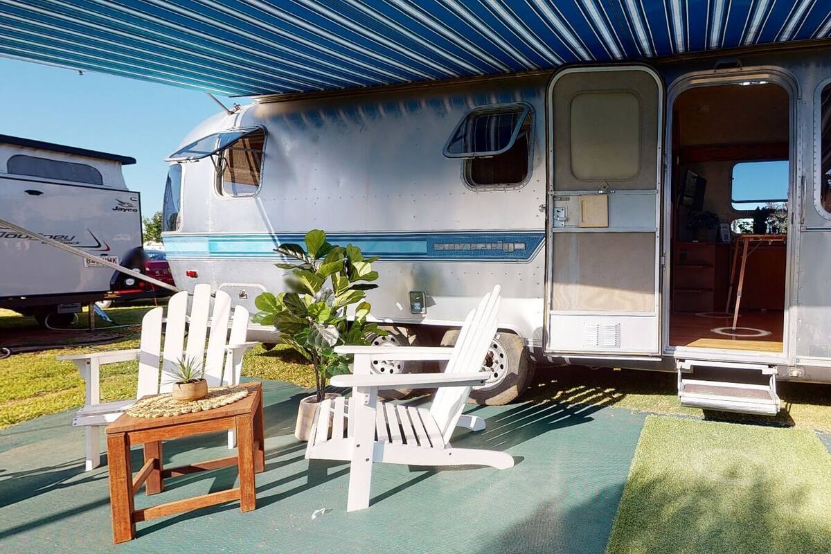 Una autocaravana con un espacio exterior cubierto, una pequeña mesa y dos sillas de jardín.