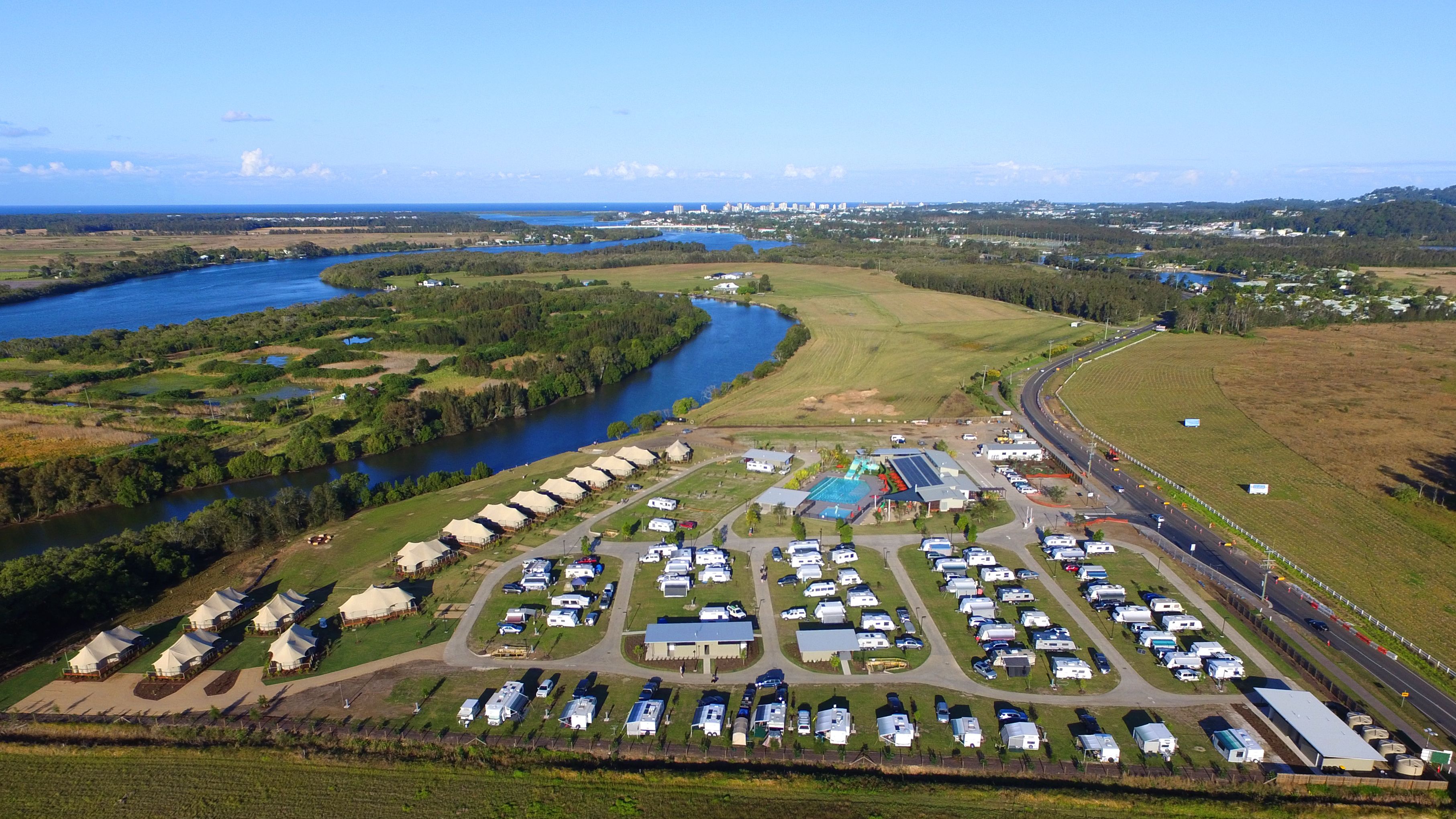 Vista aérea de um camping com veículos recreativos, tendas e piscina.