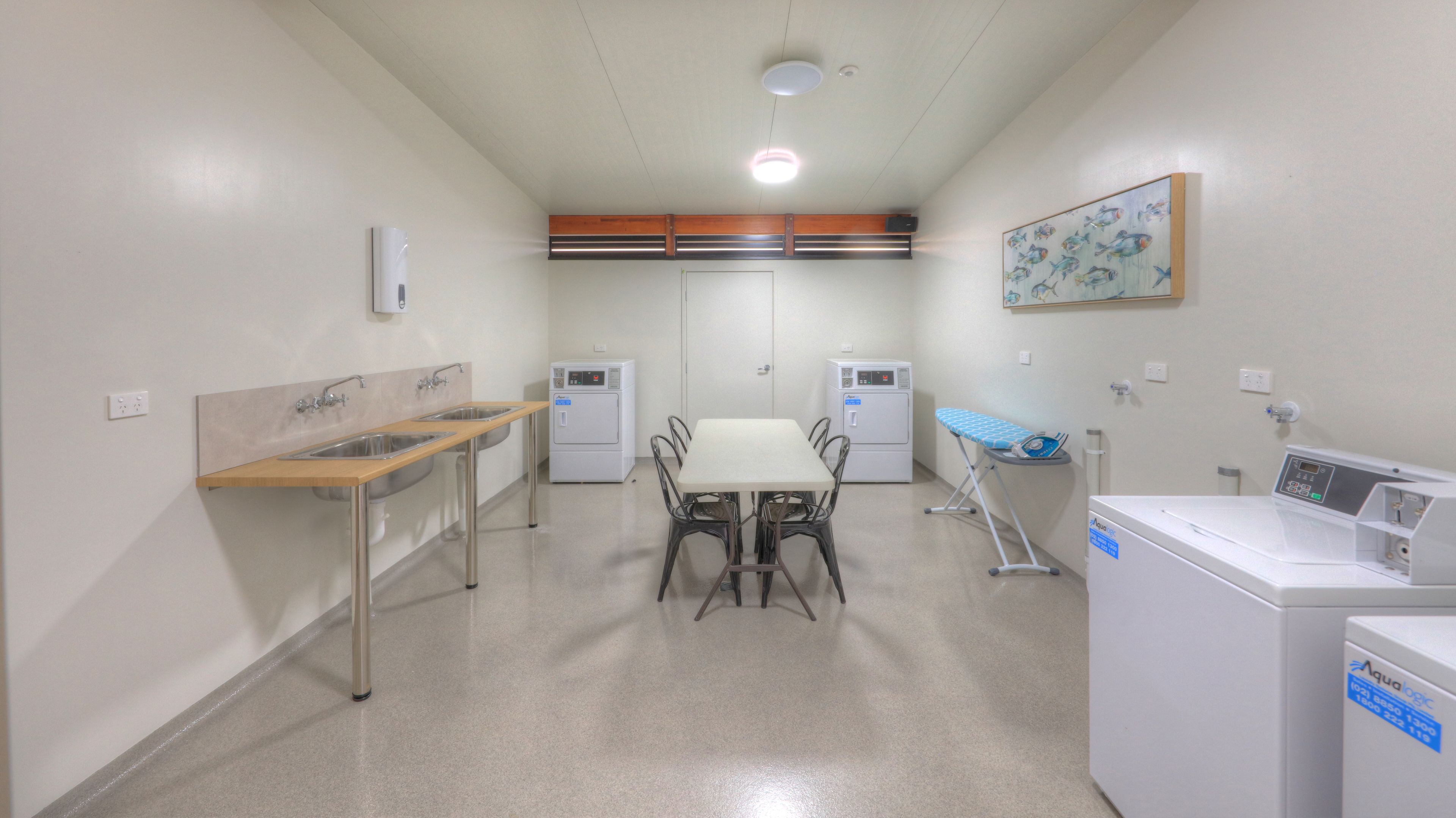 A clean, well-lit room with a table and chairs, two sinks, a drying station, and a washing machine.