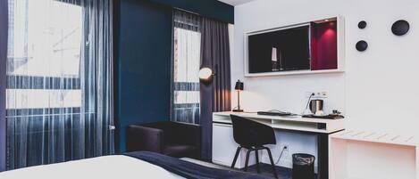 Une chambre d’hôtel moderne équipée d’un lit, d’un bureau, d’une chaise, d’une télévision et d’une fenêtre avec des rideaux.