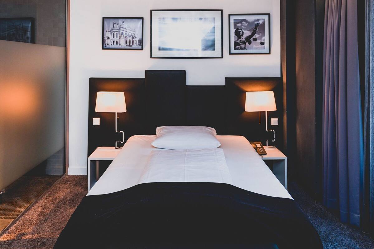 A hotel room with a bed, two bedside lamps, a telephone, and three framed pictures on the wall.