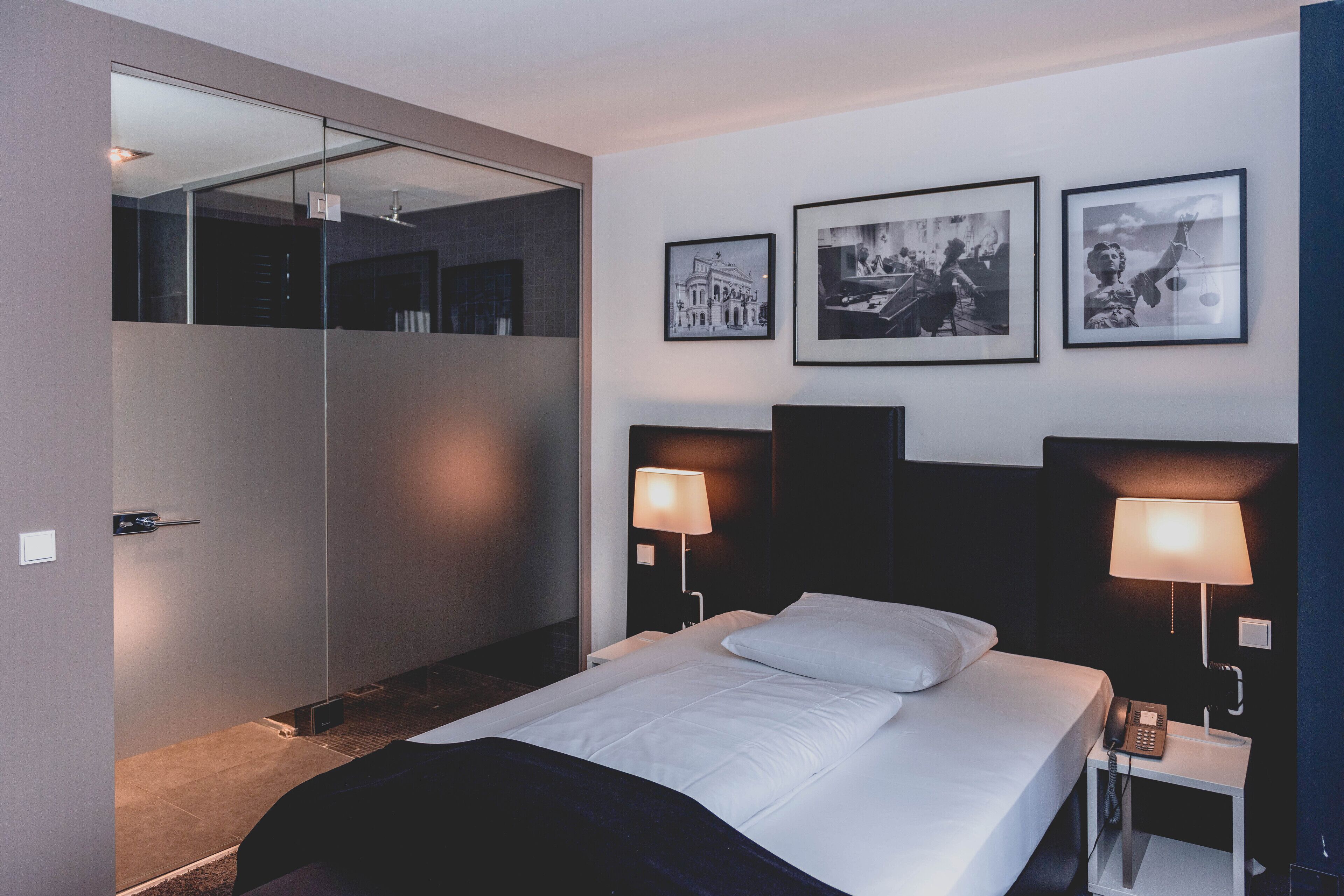 Un cuarto de hotel con una cama grande, dos mesas de noche con lámparas, un espejo y tres cuadros en la pared.