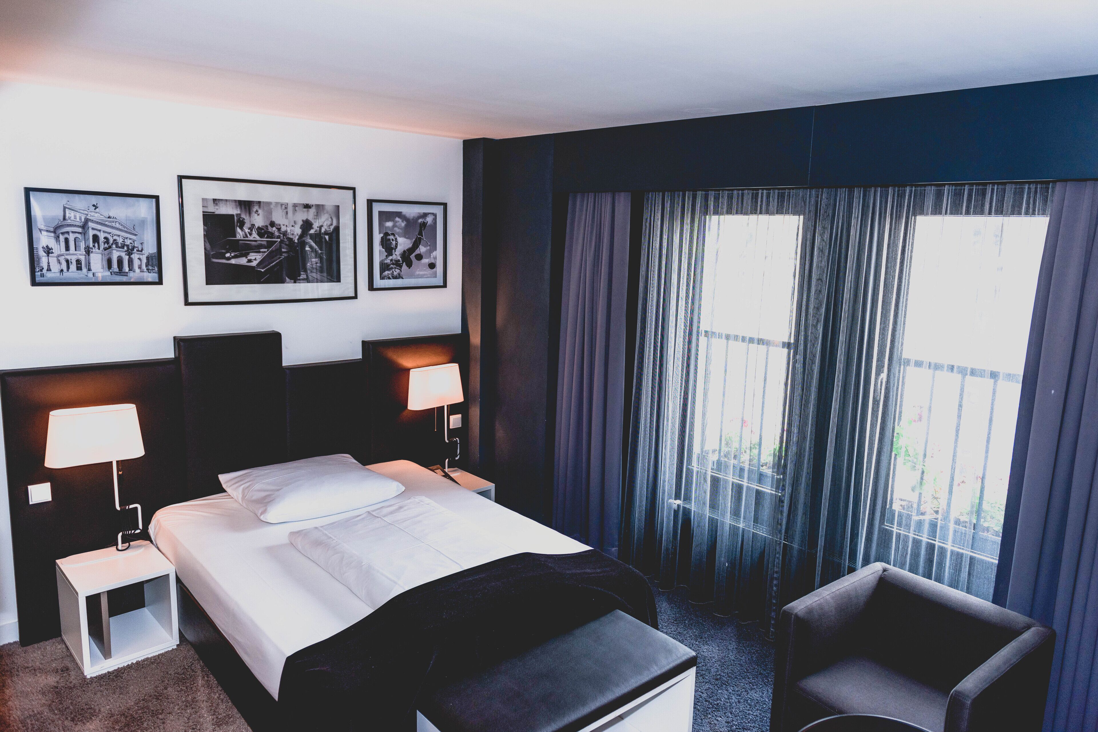 A hotel room with a bed, two bedside tables with lamps, a chair, and three framed pictures on the wall.