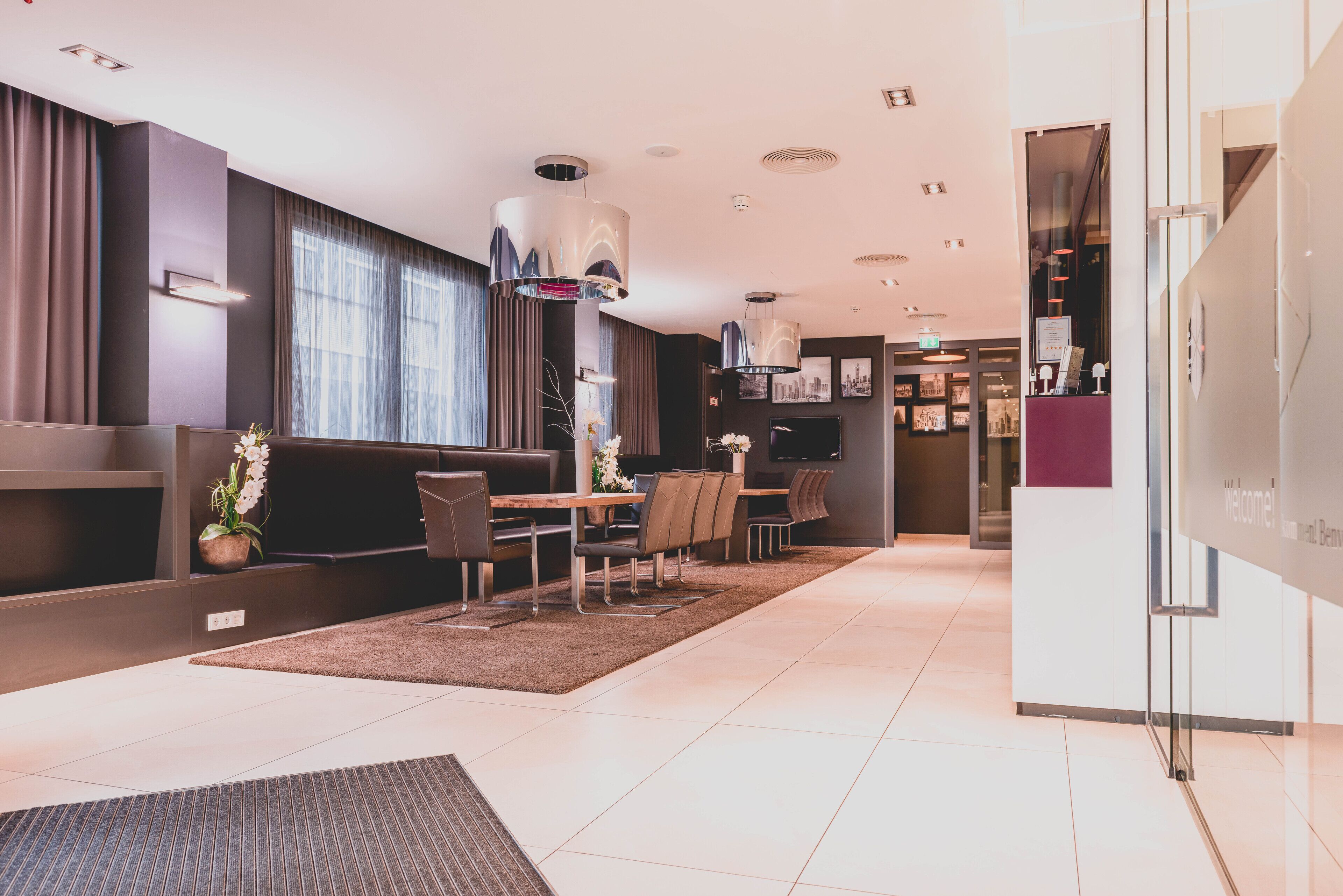 A modern hotel lobby with a reception desk, seating area, and a dining space.