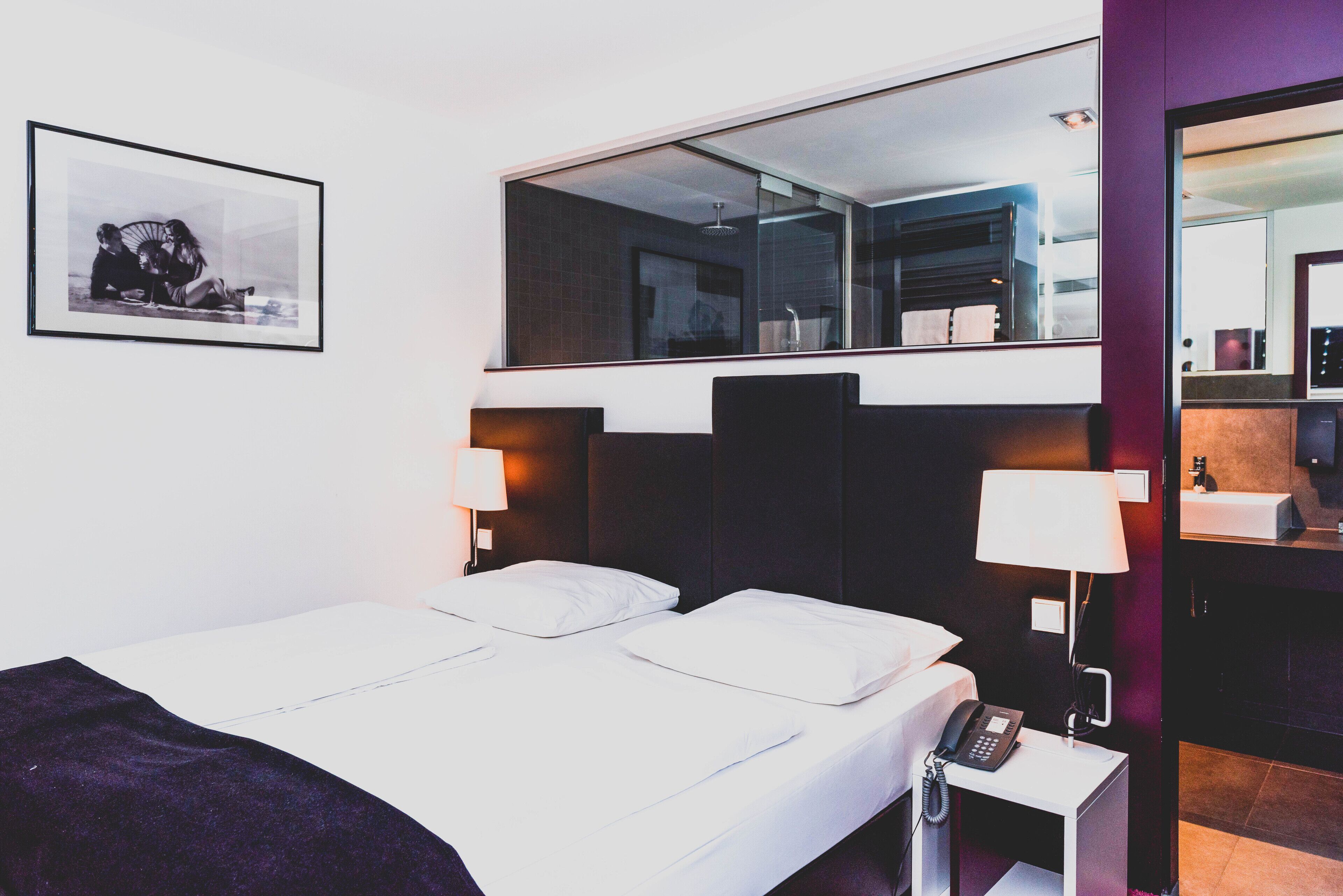 A hotel room with a bed, bedside lamps, a phone, a mirror, and a framed picture on the wall.