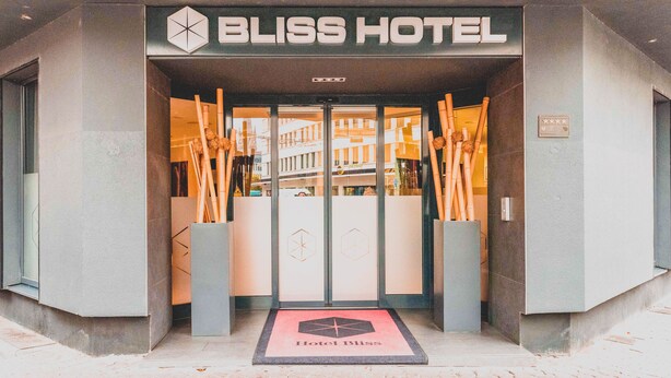The entrance to Bliss Hotel with a modern design, featuring a glass door and a doormat with the hotel's logo.
