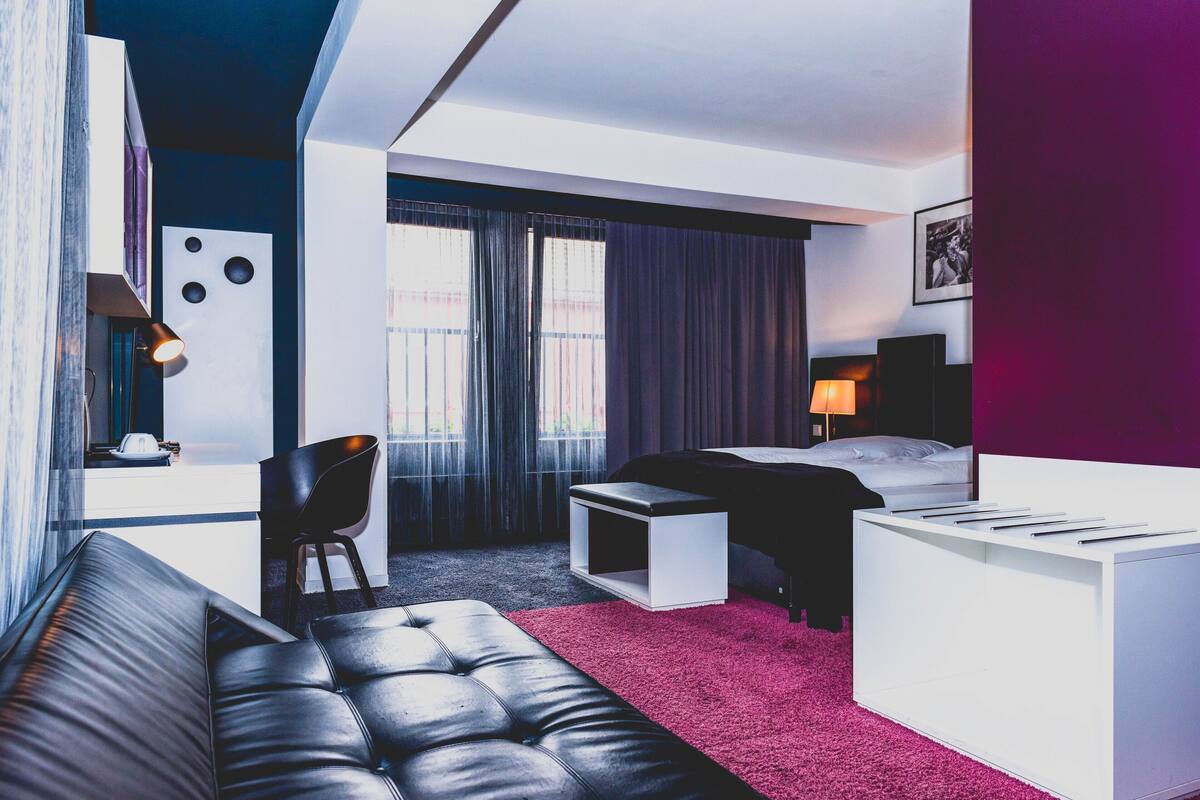 A modern hotel room with a bed, a desk, a chair, and a sofa.