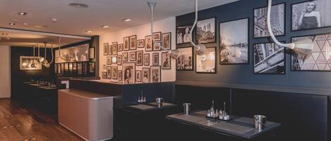 A modern restaurant with a central bar, multiple dining tables, and a wall adorned with framed photographs.
