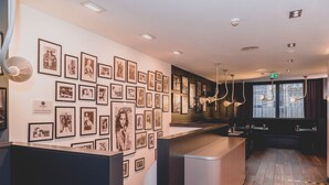 A modern hotel lobby with a long reception desk, a wall adorned with framed photographs, and a wooden floor.