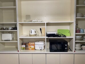 A kitchen with white cabinets, a toaster, a kettle, a rice cooker, a microwave, and a green cutting board. - Palette Takashimadaira - Hostel (Tokyo)