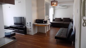 A modern living room with a flat-screen TV, a microwave, a coffee maker, and a sofa. - Palette Takashimadaira - Hostel (Tokyo)