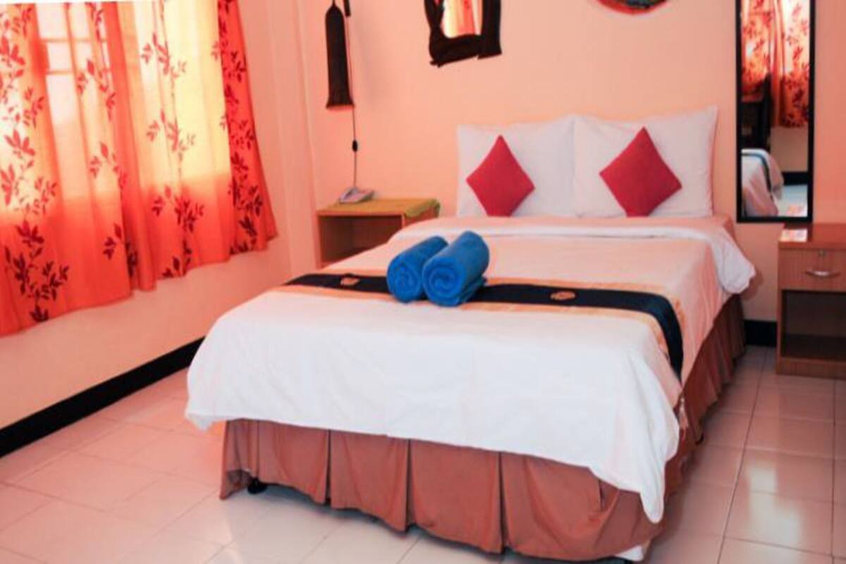 A hotel room with a bed, a nightstand, a mirror, and a window with curtains.