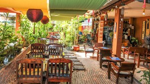 An outdoor seating area with wooden furniture, potted plants, and a brick pathway. - All In 1 Guesthouse Chiang Mai (Chiang Mai)