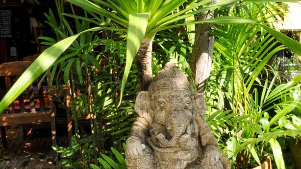 A statue of a deity seated on a pedestal surrounded by lush greenery. - All In 1 Guesthouse Chiang Mai (Chiang Mai)