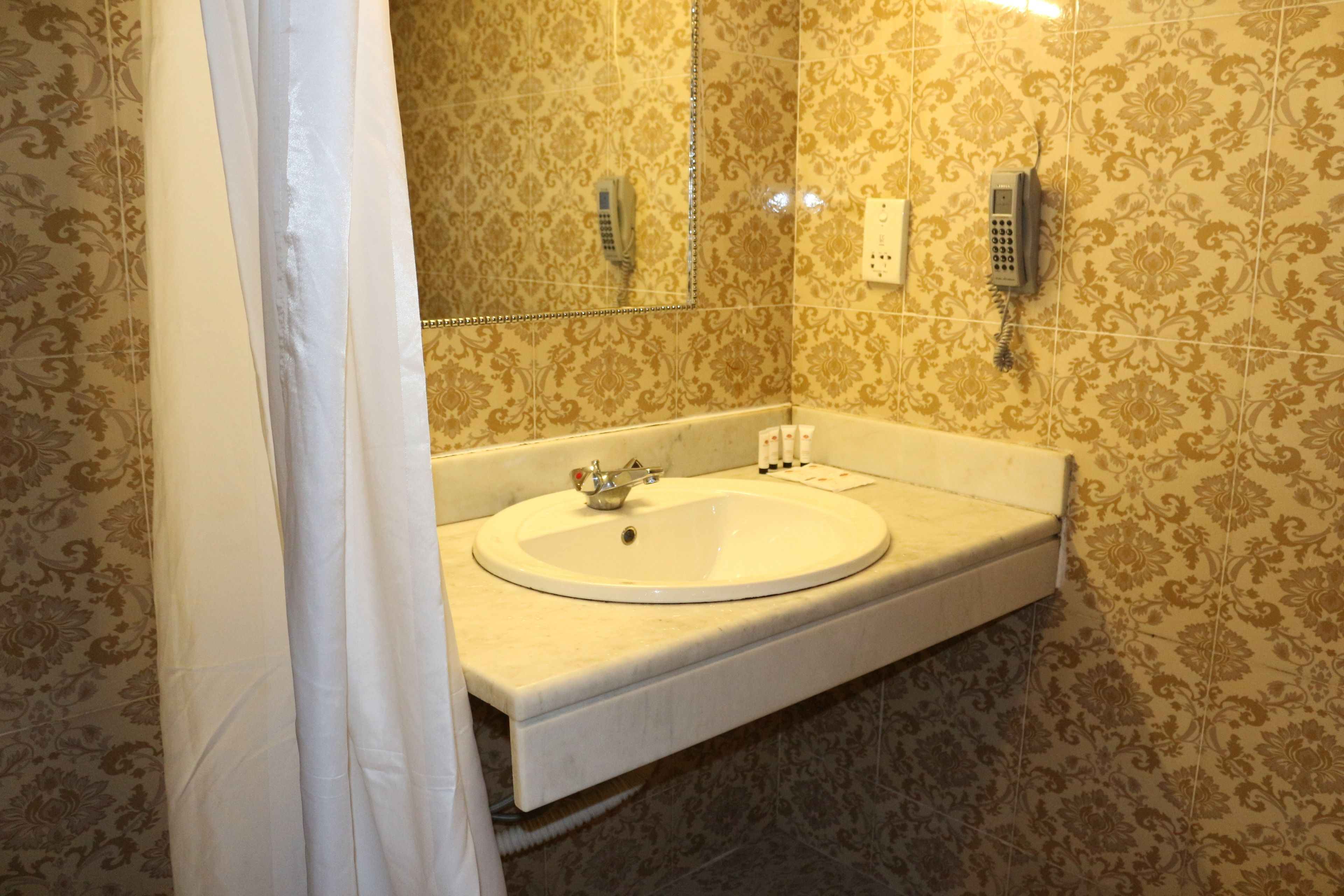 A bathroom with a white sink, a mirror, and two phones mounted on the wall.