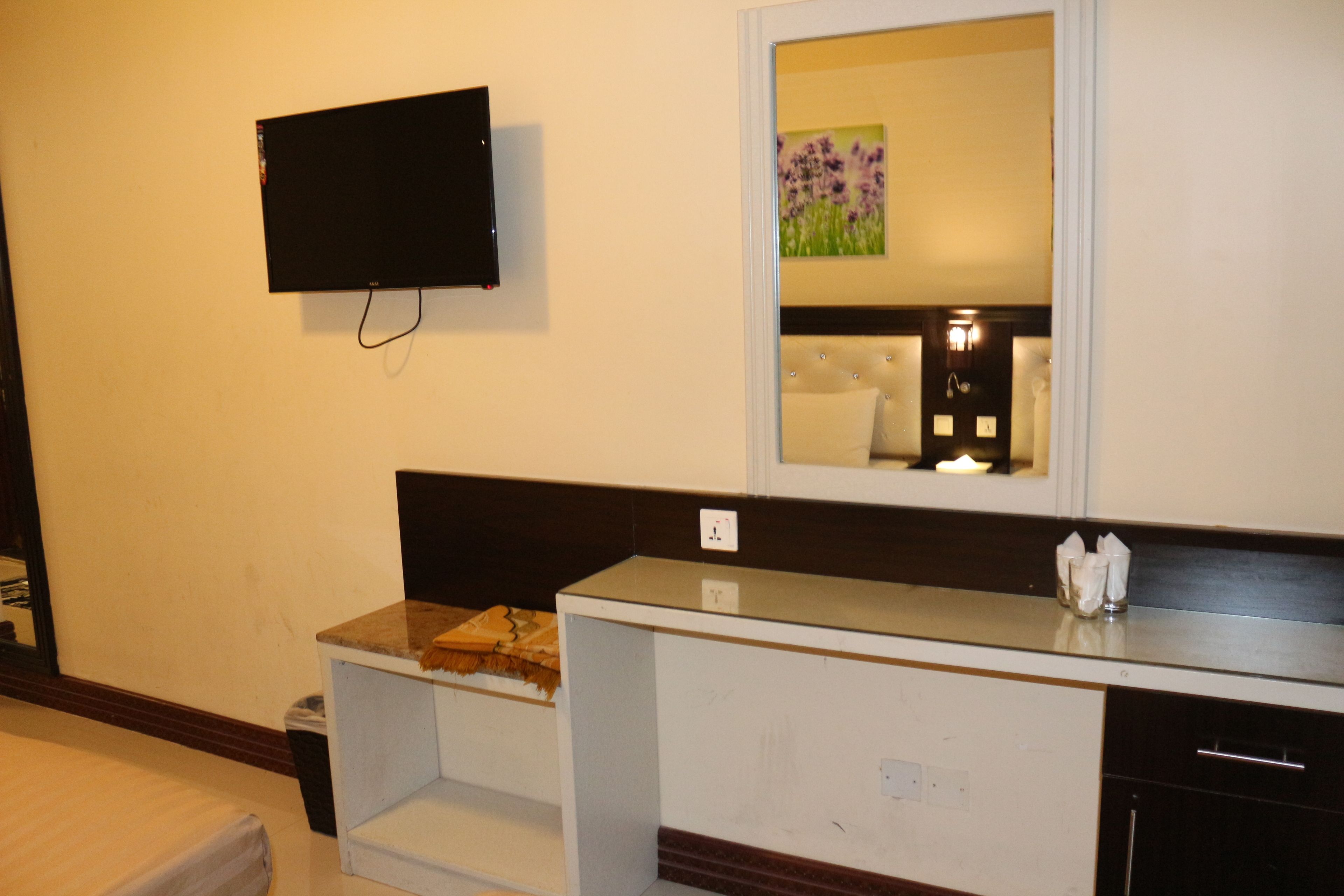 A hotel bathroom with a flat-screen TV mounted on the wall, a mirror above the sink, and a small decorative item on the counter.