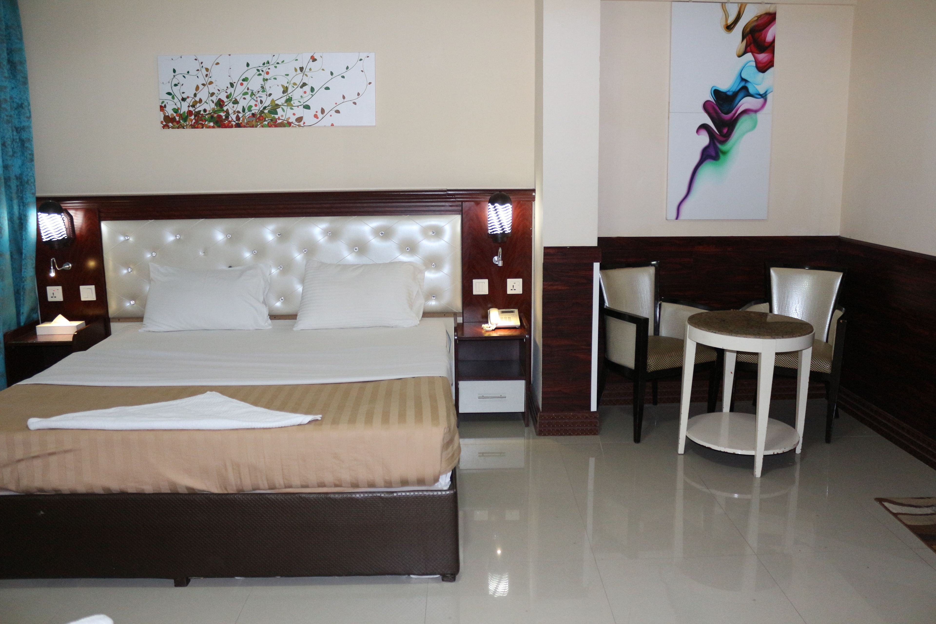 A hotel room with a large bed, bedside tables, a small round table with two chairs, and artwork on the walls.
