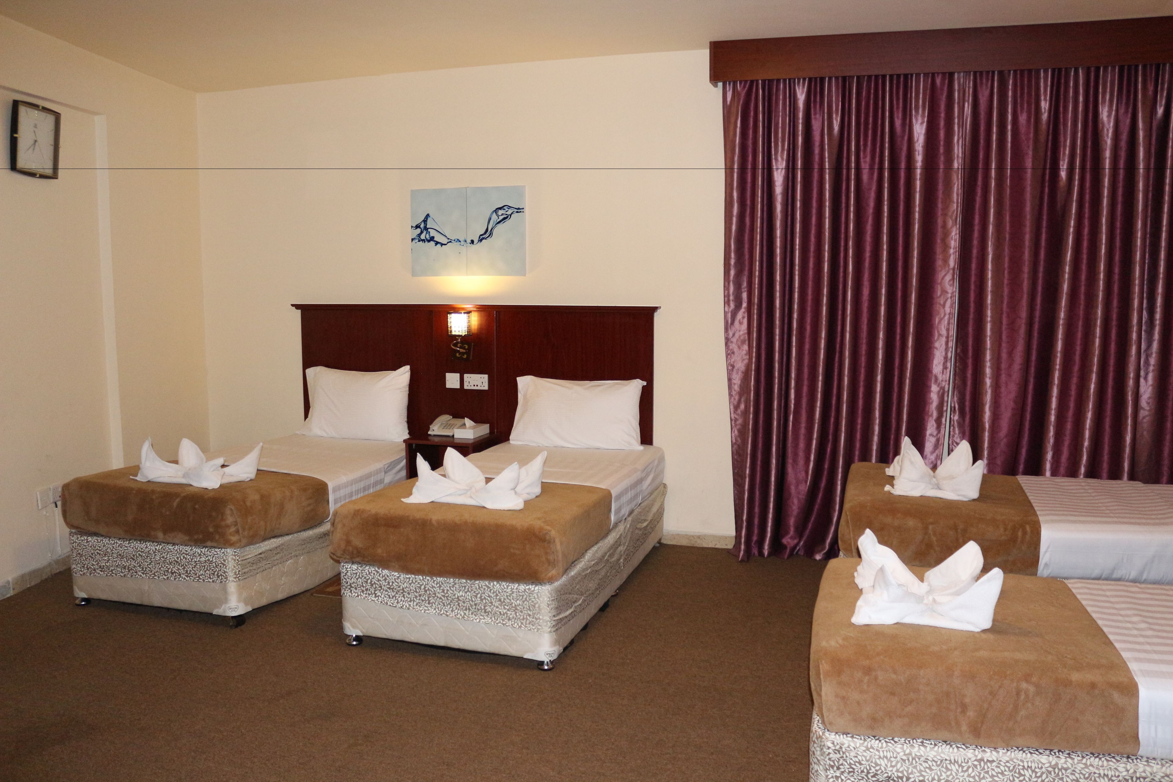 A hotel room with two beds, a wooden headboard, a nightstand, and a large window with a curtain.