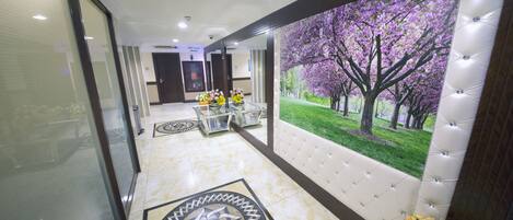 A hotel lobby with a large mural of a tree and flowers, a glass partition, a reception desk, and a patterned floor design.