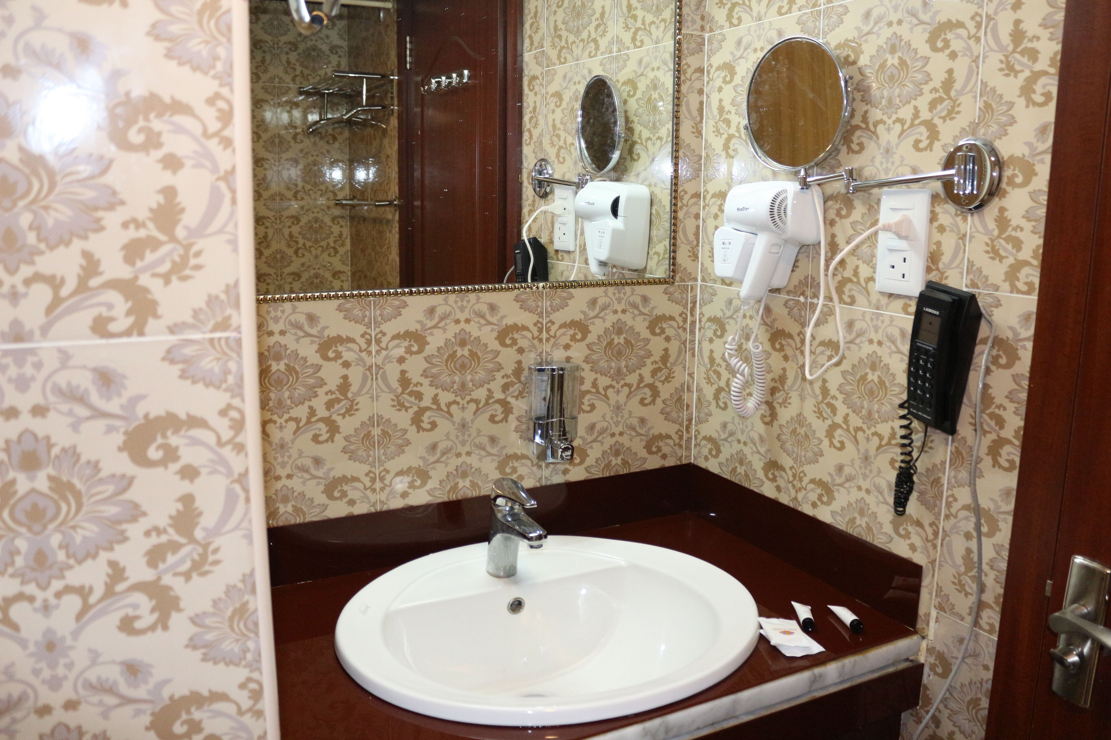A bathroom with a marble sink, two mirrors, a hairdryer, and a telephone.