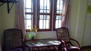 A room with a table and two chairs, a window with curtains, and a potted plant on the table. - Royal Flower Guest House (Pyin Oo Lwin)