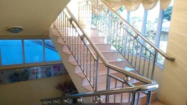 A staircase with metal railings and a view of the outside through a window. - Royal Flower Guest House (Pyin Oo Lwin)