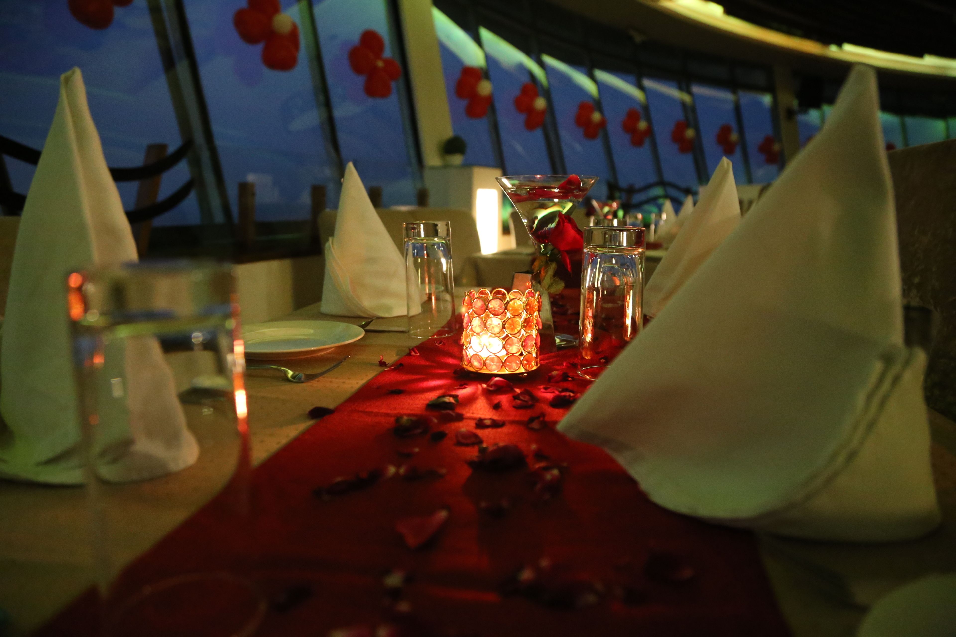 A table set for a meal with a red table runner, glasses, a candle, and napkins.