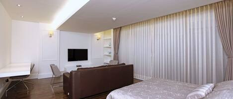 Een moderne hotelkamer met een groot bed, een zithoek met een bank, een bureau en een wandgemonteerde flatscreen televisie.