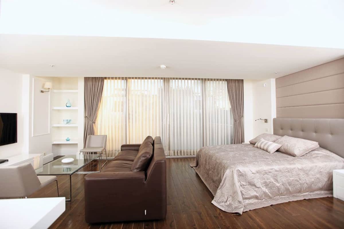 A modern hotel room with a sofa, a bed, a glass coffee table, and a TV.