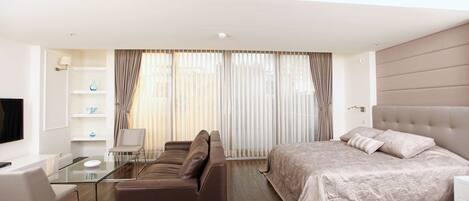 A modern hotel room with a sofa, a bed, a glass coffee table, and a TV.