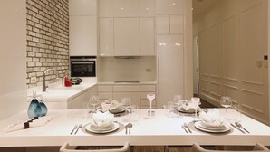 A modern dining area with a long table set for a meal, a kitchen area with white cabinetry, and a brick accent wall. - Pera Residence (Istanbul)