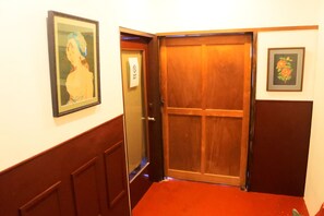 A hallway with a wooden door, a framed picture on the wall, and a red carpet. - Retro Boy Coffee (Yuni)