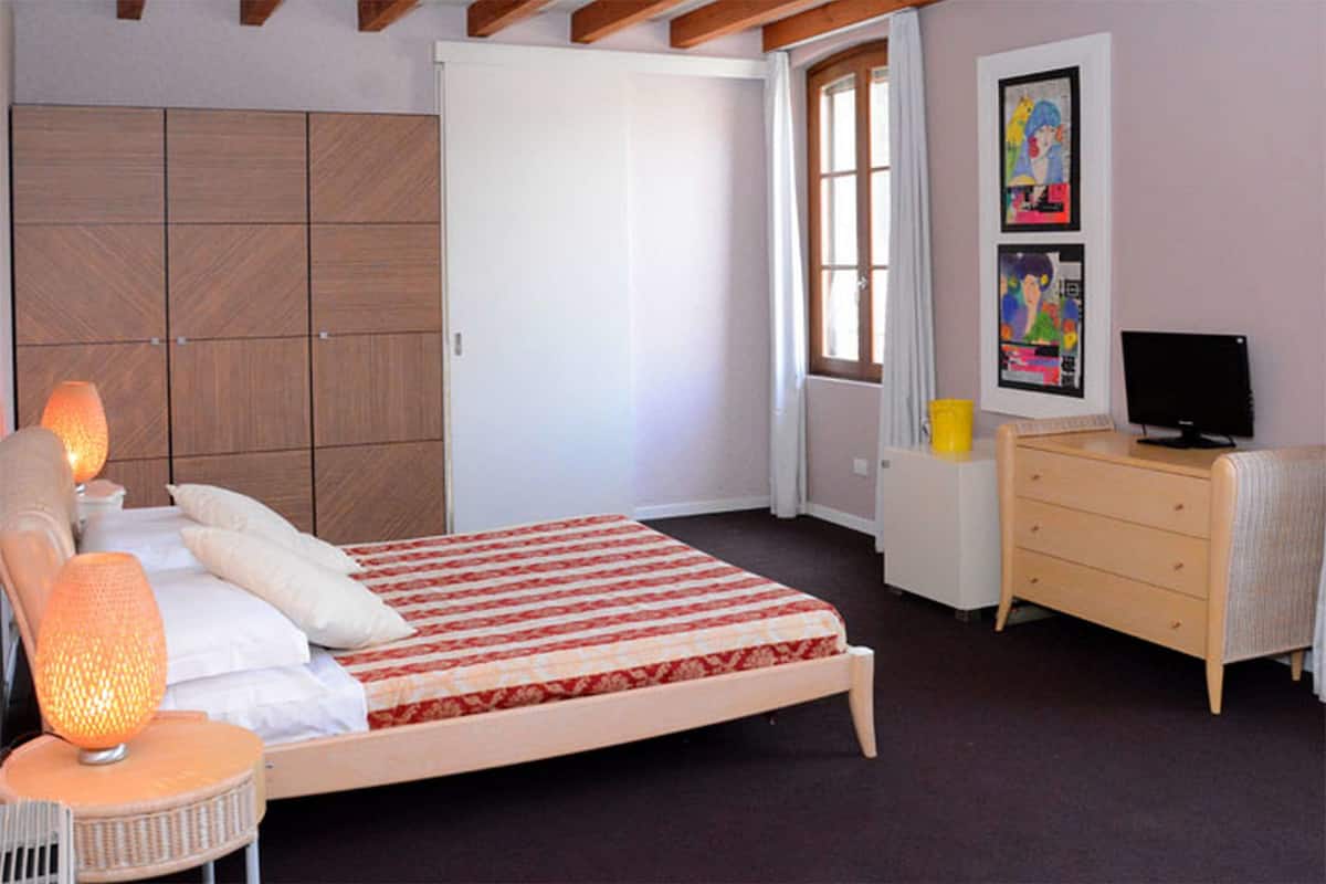 A bedroom with a bed, bedside lamps, a dresser, a television, and artwork on the wall.