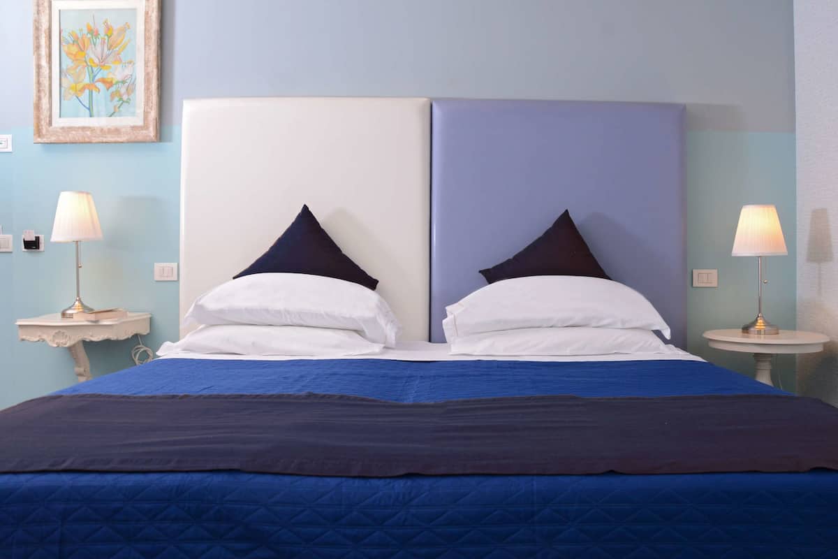 A double bed with a blue quilt, two white pillows, and a dark blue headboard. There are two bedside tables with lamps.
