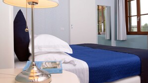 A neatly made bed with a blue bedspread, a white pillow, and a white pillow on the side. A lamp with a white shade is on a bedside table, and a map is visible on the table. - Agriturismo Ponte di Rialto (Crema)