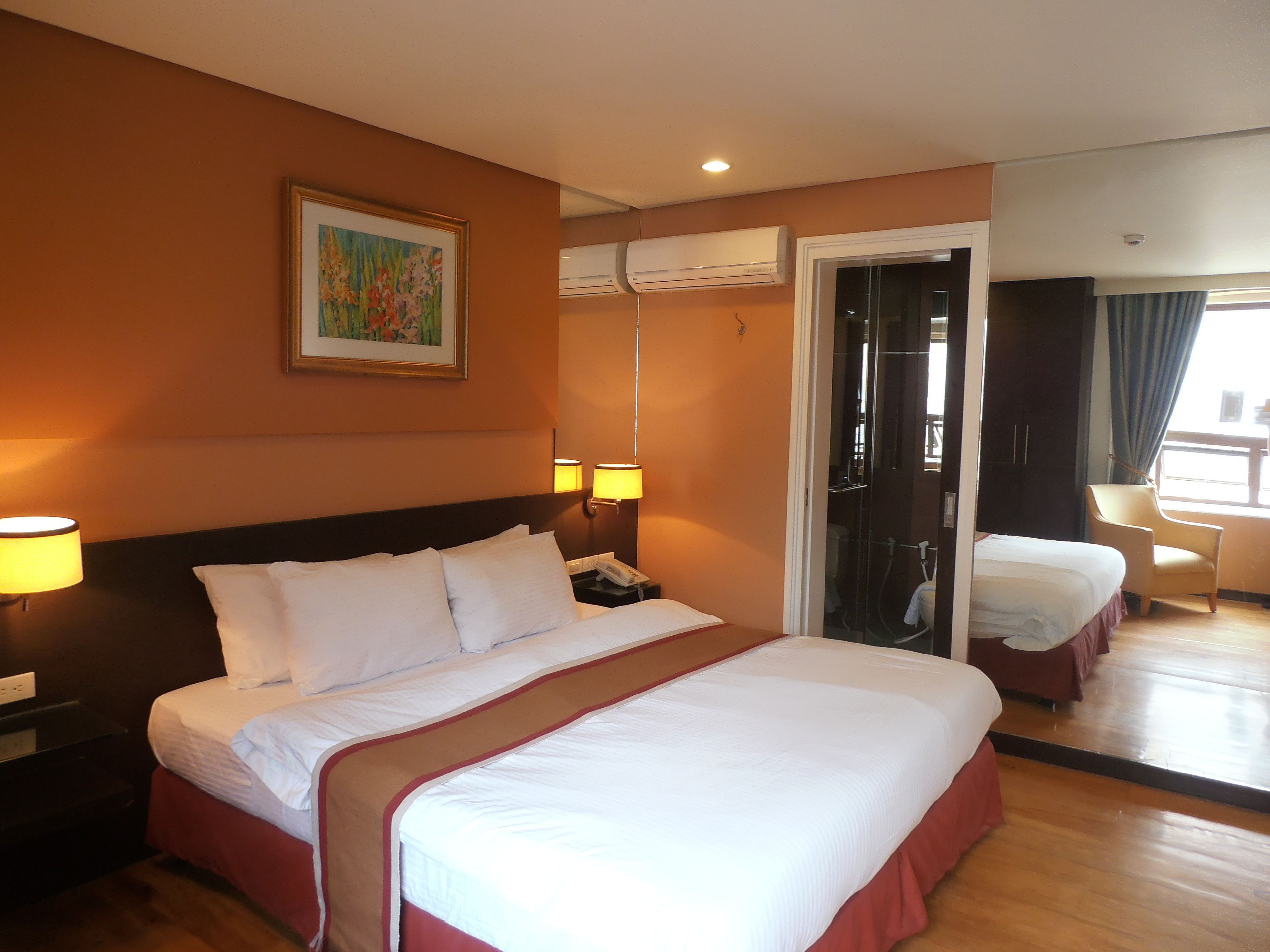 Une chambre d’hôtel avec un grand lit, des lampes de chevet, un appareil de climatisation, un tableau au mur et une vue sur l’extérieur par une porte.