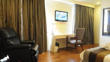 Ein Hotelzimmer mit schwarzem Ledersessel, Schreibtisch inklusive Computer, Wand-TV und einem Bett mit gesteppter Decke.