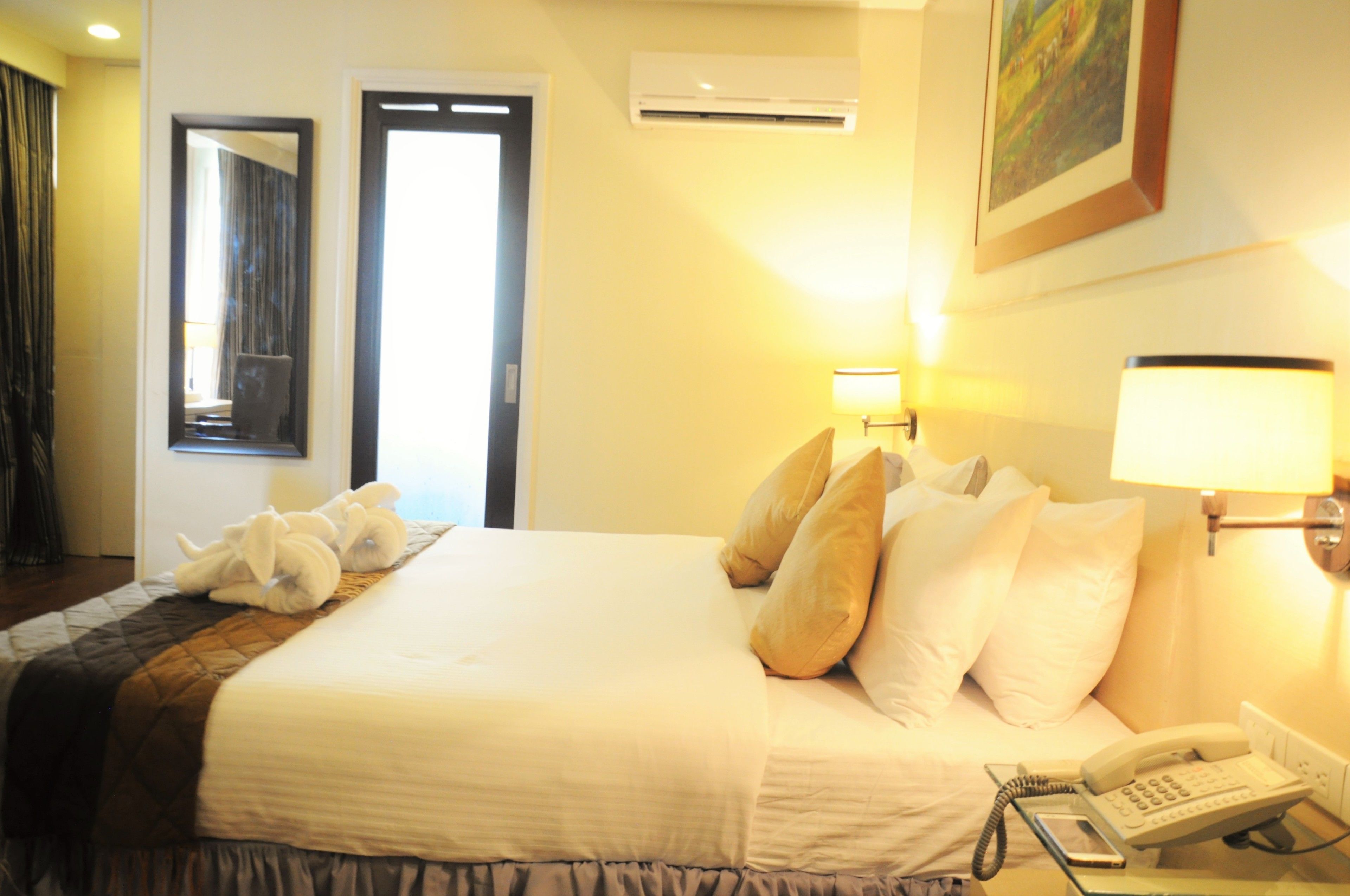Habitación de hotel con cama, almohadas, lámpara de noche, teléfono y aire acondicionado.