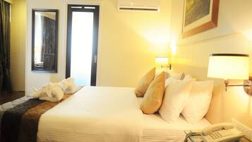 Habitación de hotel con cama, almohadas, lámpara de noche, teléfono y aire acondicionado.