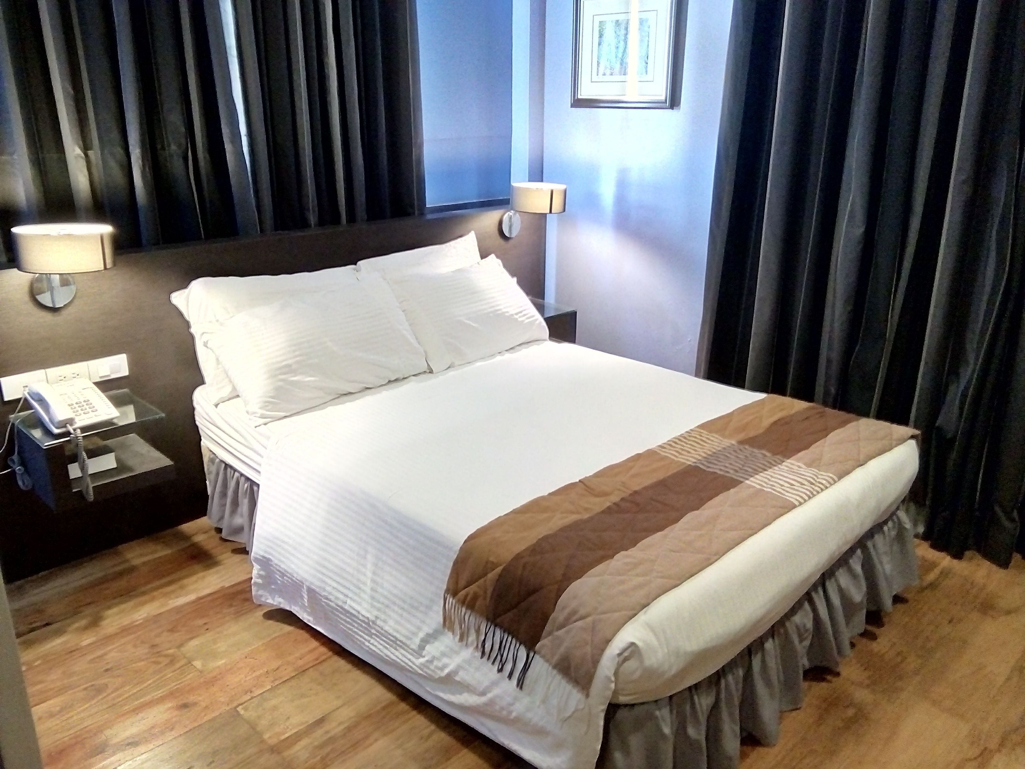 Hotellihuone, jossa on suuri sänky, kaksi yöpöytälamppua, puhelin ja seinällä oleva kehystetty kuva.