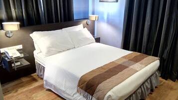 Hotellihuone, jossa on suuri sänky, kaksi yöpöytälamppua, puhelin ja seinällä oleva kehystetty kuva.