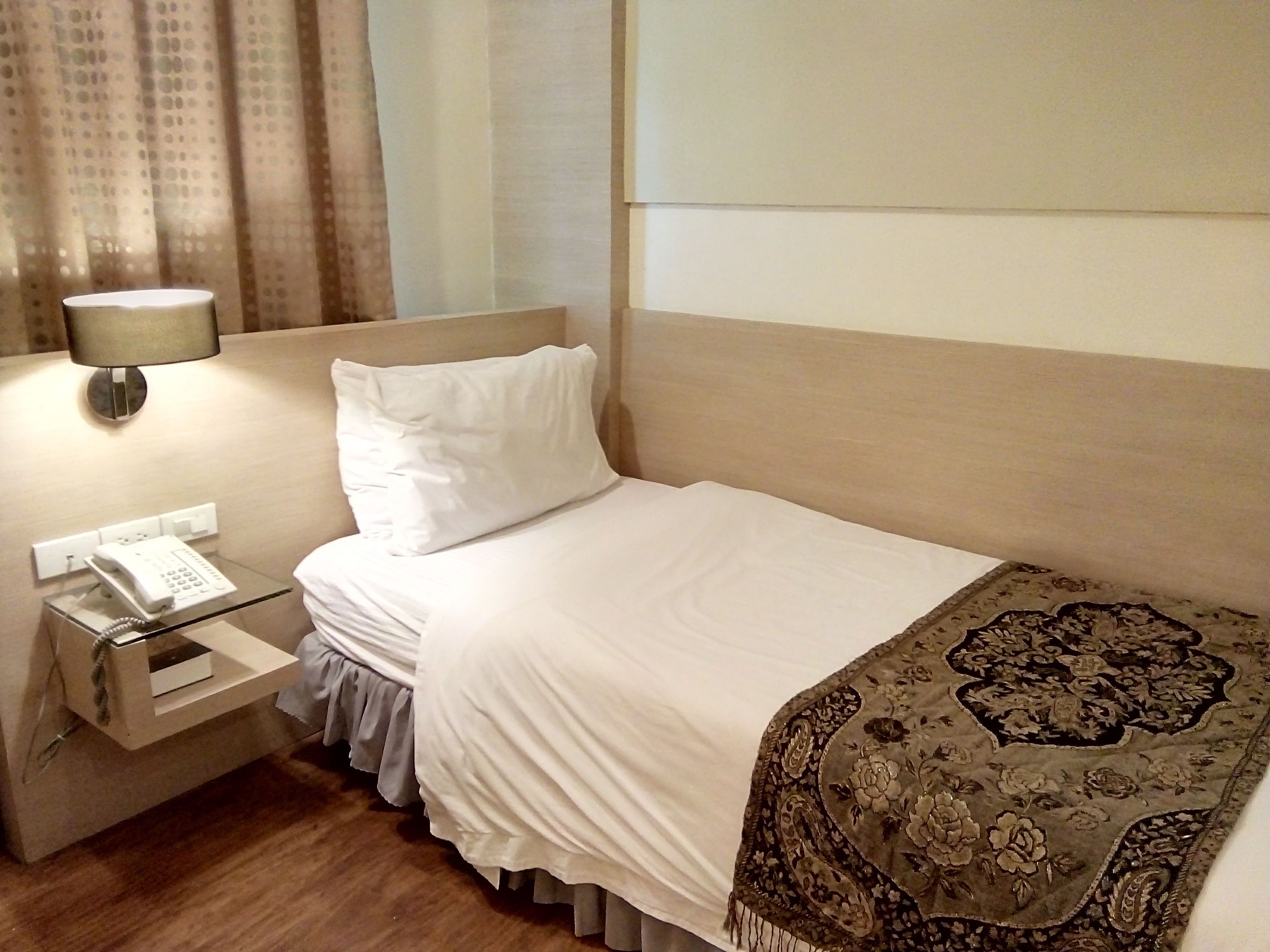 Quarto de hotel com uma cama, um telefone de apoio e uma luminária.