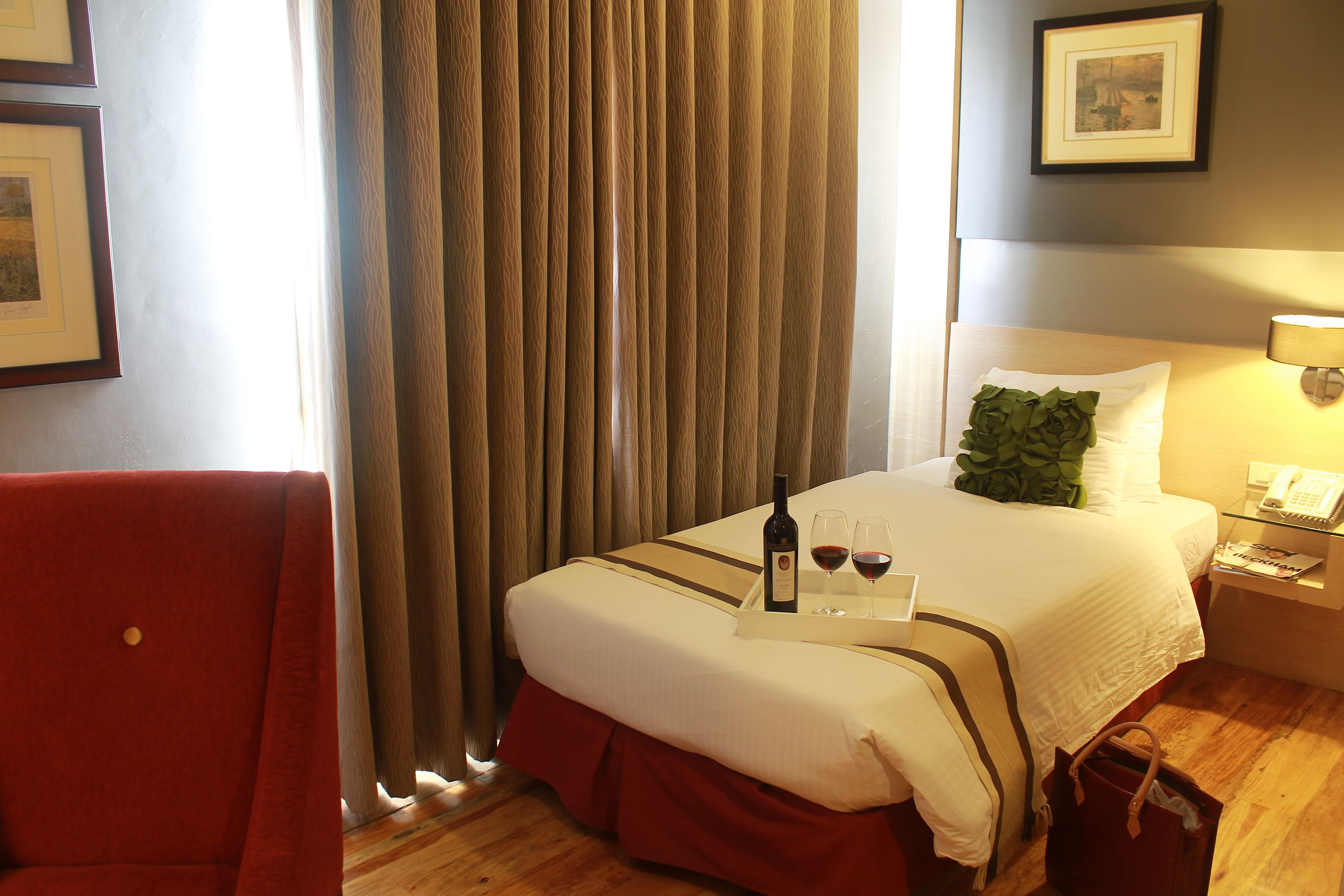 Una habitación de hotel con una cama, una mesita de noche, una silla, una cortina y un cuadro en la pared.