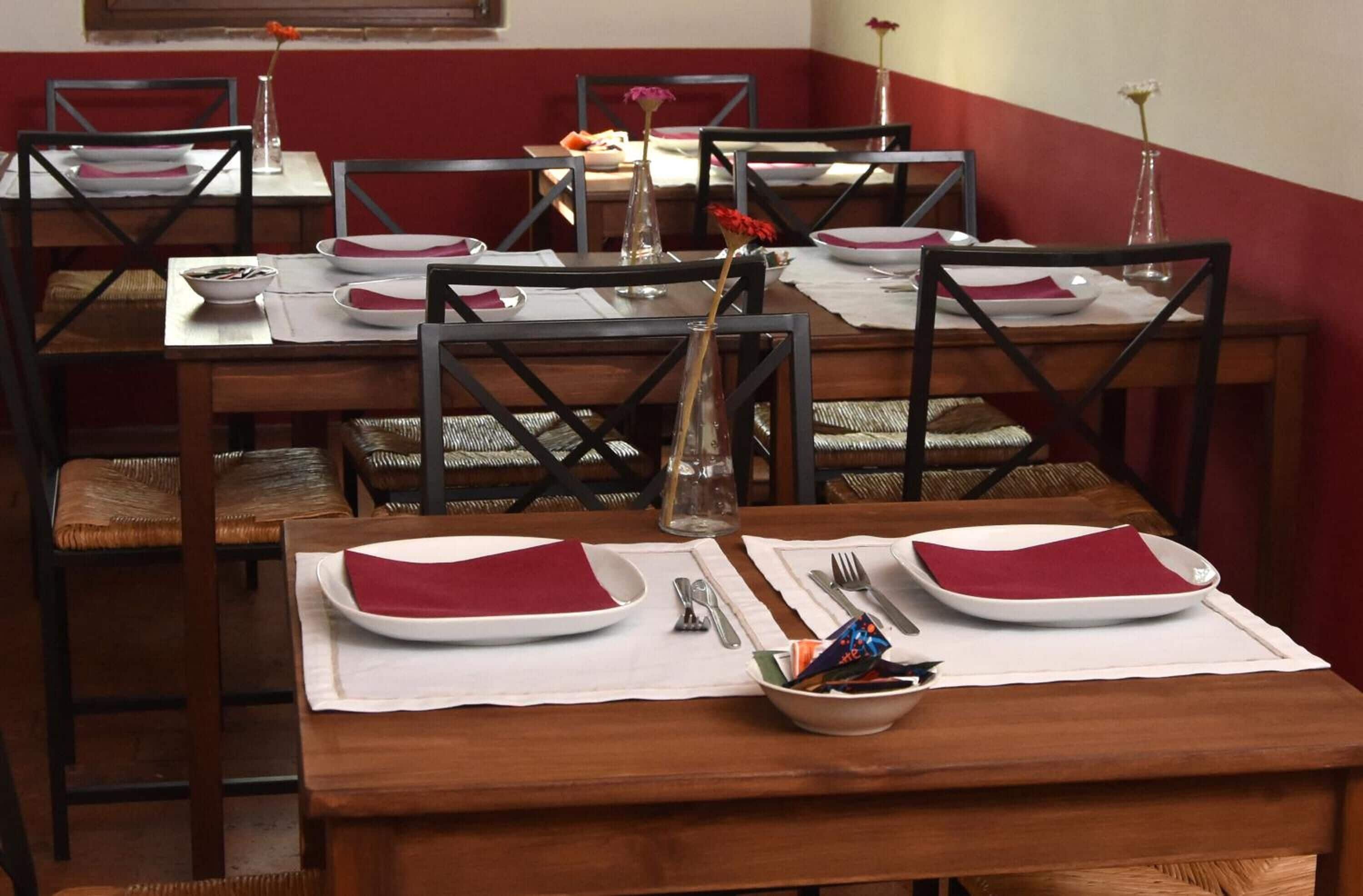 A dining area with wooden tables and chairs, white placemats, and red napkins.