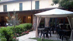 An outdoor patio with tables and chairs, a covered seating area, and a garden with potted plants and flowers. - Albergo Antica Hostelleria (Crema)