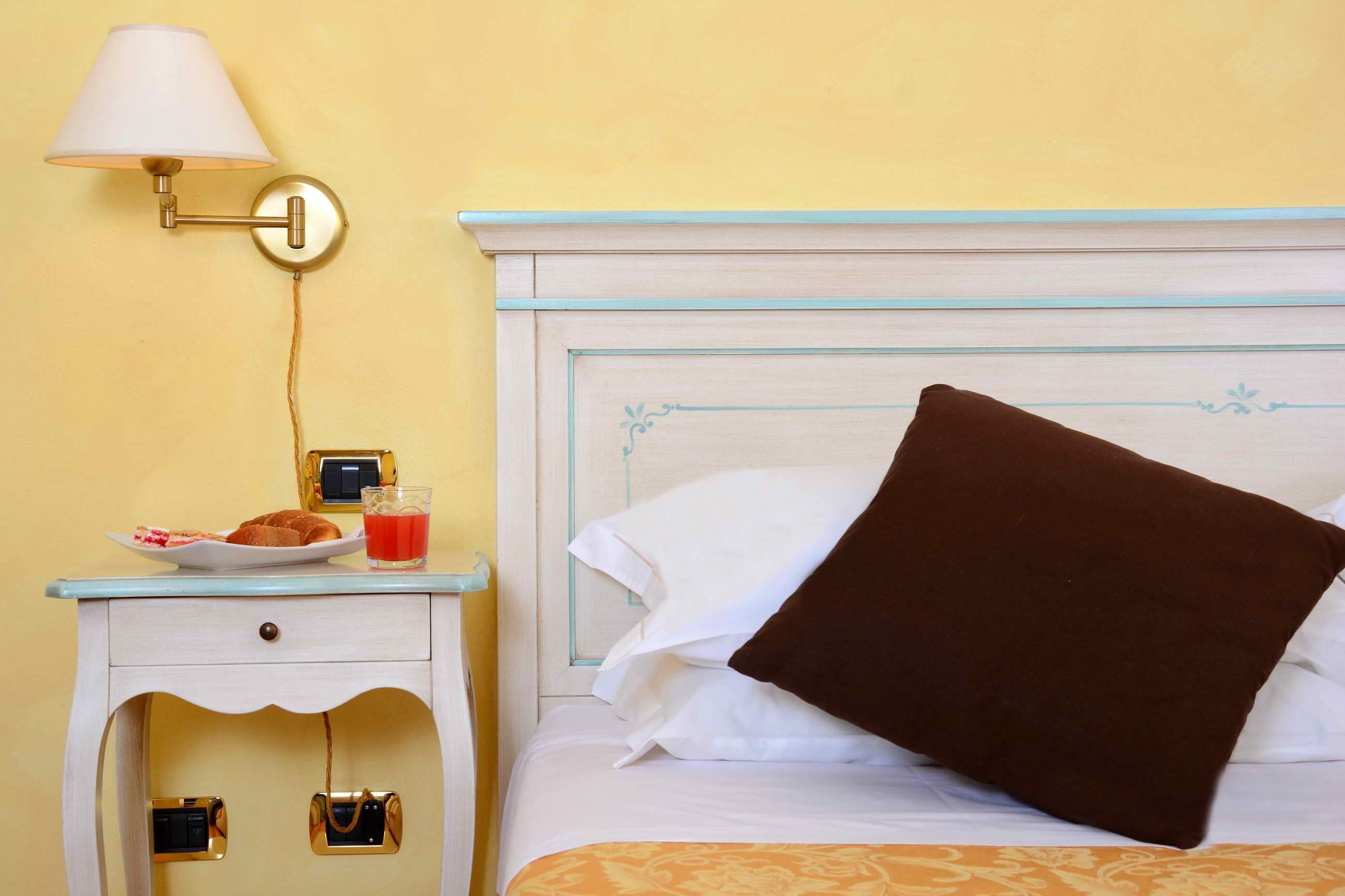 Une chambre d’hôtel avec un lit, une table de chevet avec une lampe, une assiette de nourriture et un verre de jus de fruits.