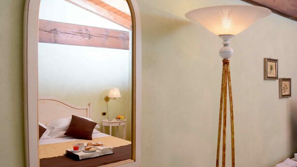 A hotel room with a bed, a bedside table with a lamp, and a mirror reflecting the room. - Albergo Antica Hostelleria (Crema)