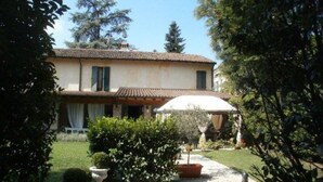 A two-story house with a tiled roof, a covered patio, and a garden with various plants and a pathway. - Albergo Antica Hostelleria (Crema)