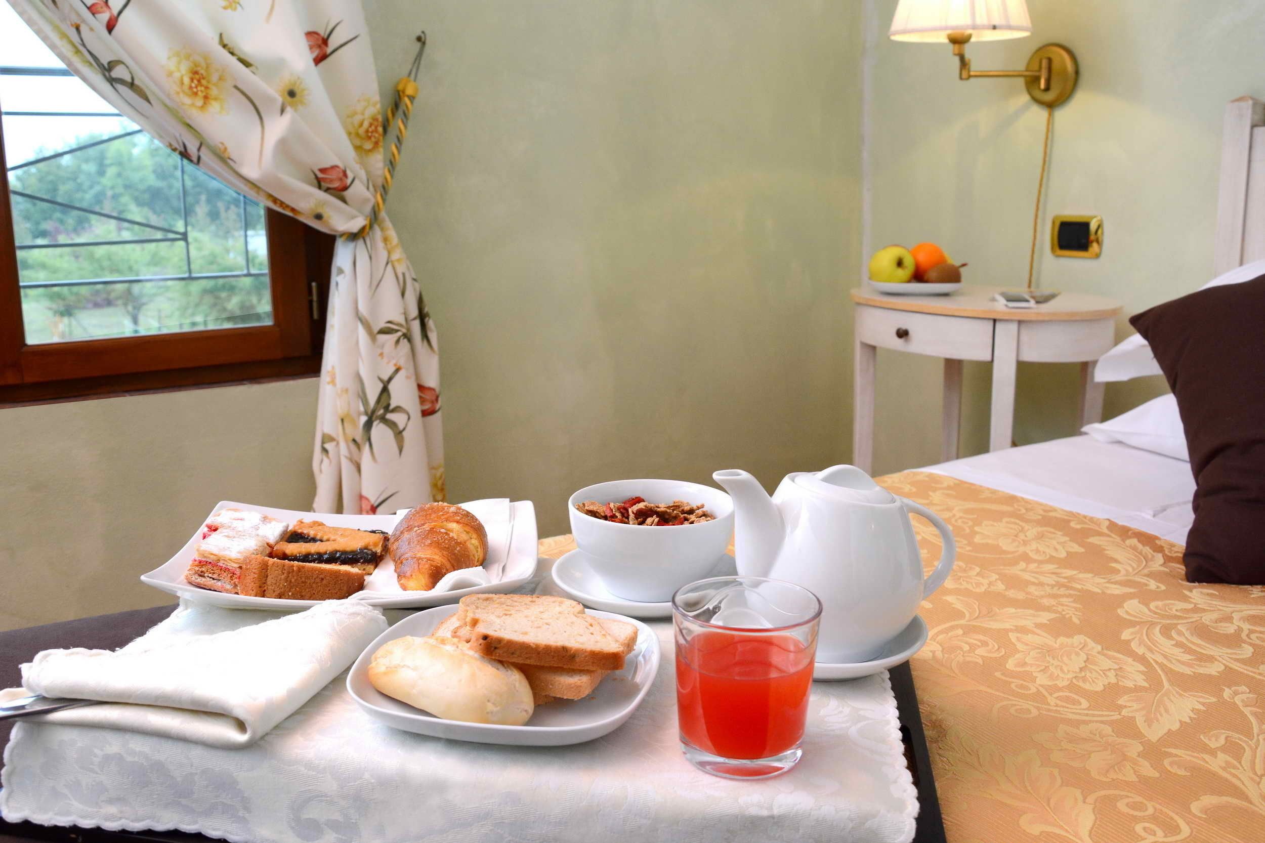 Una mesa de desayuno bien ordenada con pasteles, pan, un tazón de cereal, una tetera y un vaso de bebida roja.