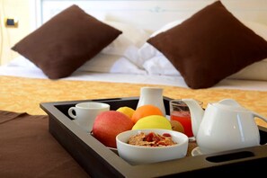 Bandeja de desayuno con frutas, una jarrón, una taza y un tazón sobre una cama con almohadas.